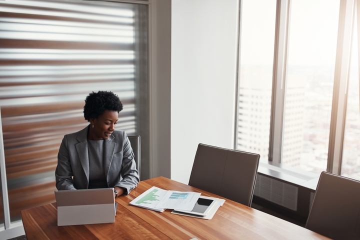 Bank professional seated at a conference table reviewing printed reports and a laptop near large office windows, symbolizing streamlined meeting preparation supported by AI insights.