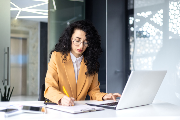 A person develops strategies to manage deflation. They have a laptop open in front of them to research and they are writing notes on a clipboard.